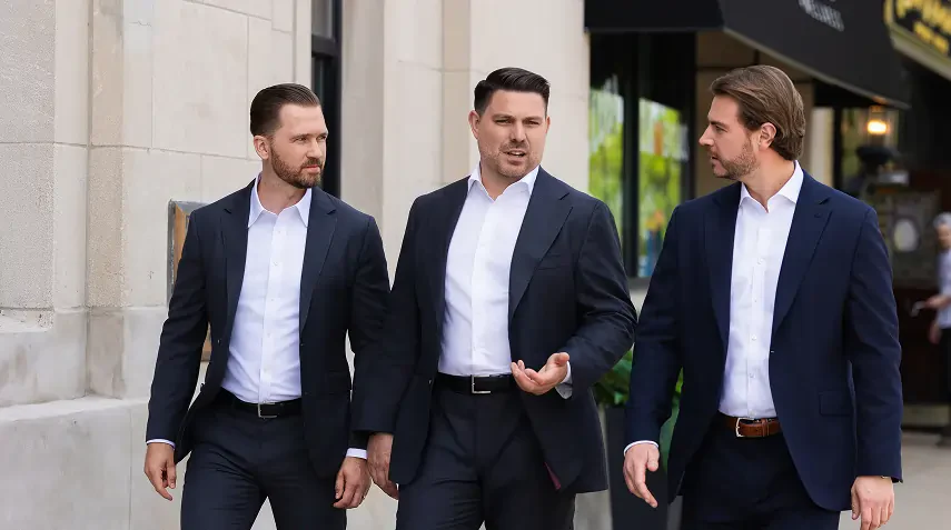 Joseph D. Mallek, Ronald Chapman II, and John J. Dowling III in business suits walking and talking on an urban sidewalk with buildings and shops in the background.