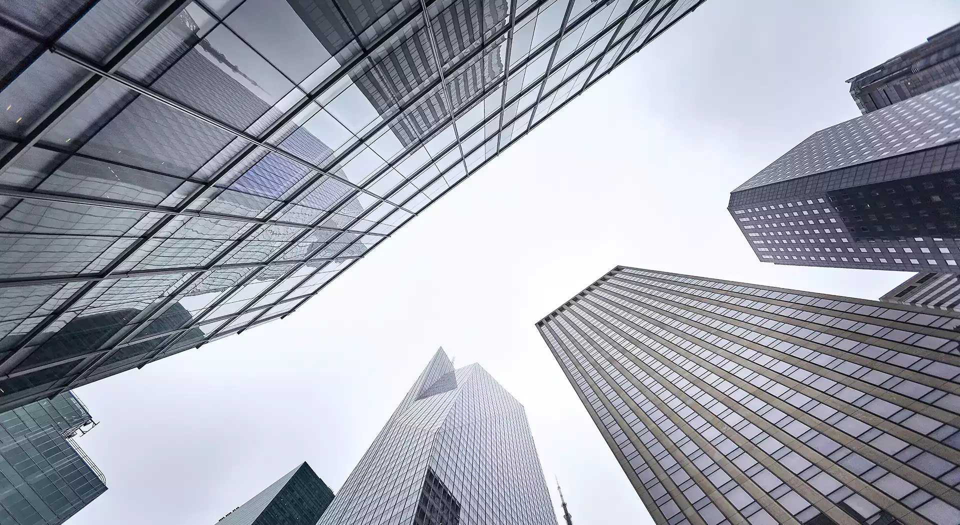 Upward view of modern glass and steel skyscrapers converging against a gray, overcast sky.